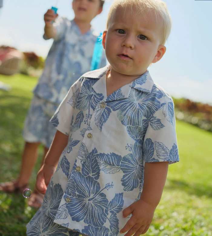 Child wearing a blue floral shirt standing outdoors on grass