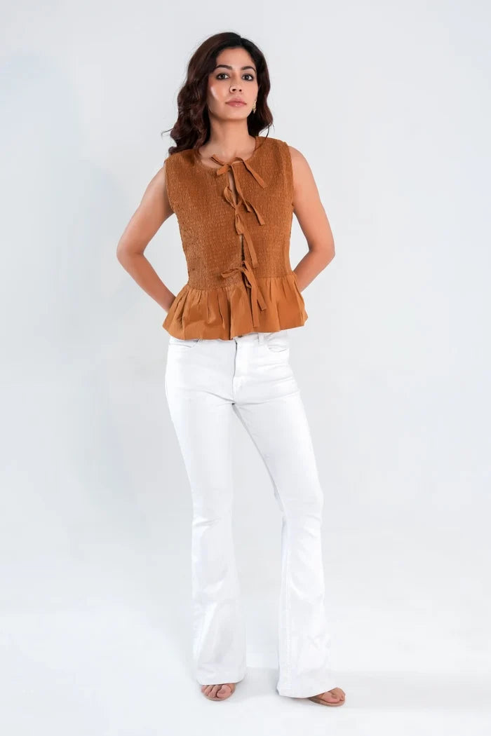 Woman wearing brown sleeveless top with smocked bodice, tie-front closure, and flowy peplum hem – front view