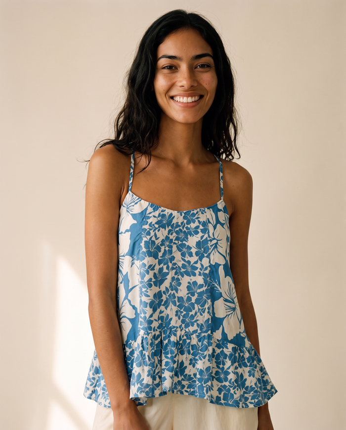 A smiling woman with dark hair wearing a blue and white floral print spaghetti-strap top, standing against a warm beige background.