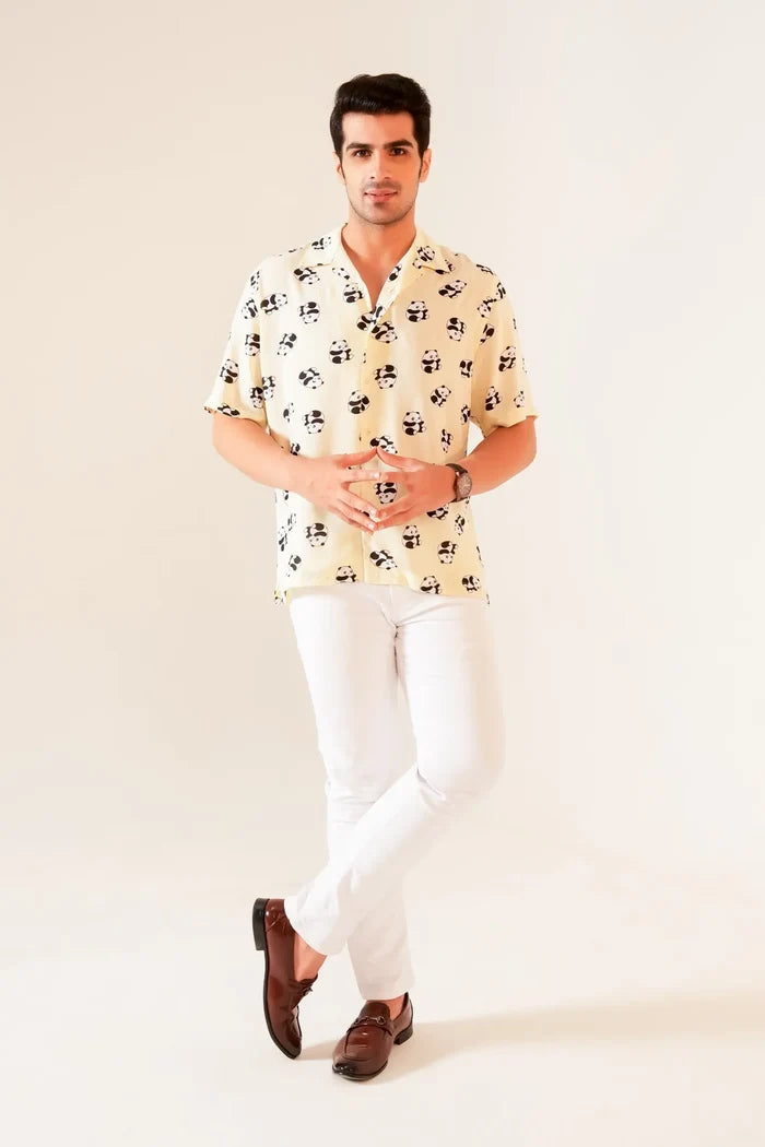 Full front view of man wearing yellow panda print oversized summer shirt styled with white pants and brown loafers
