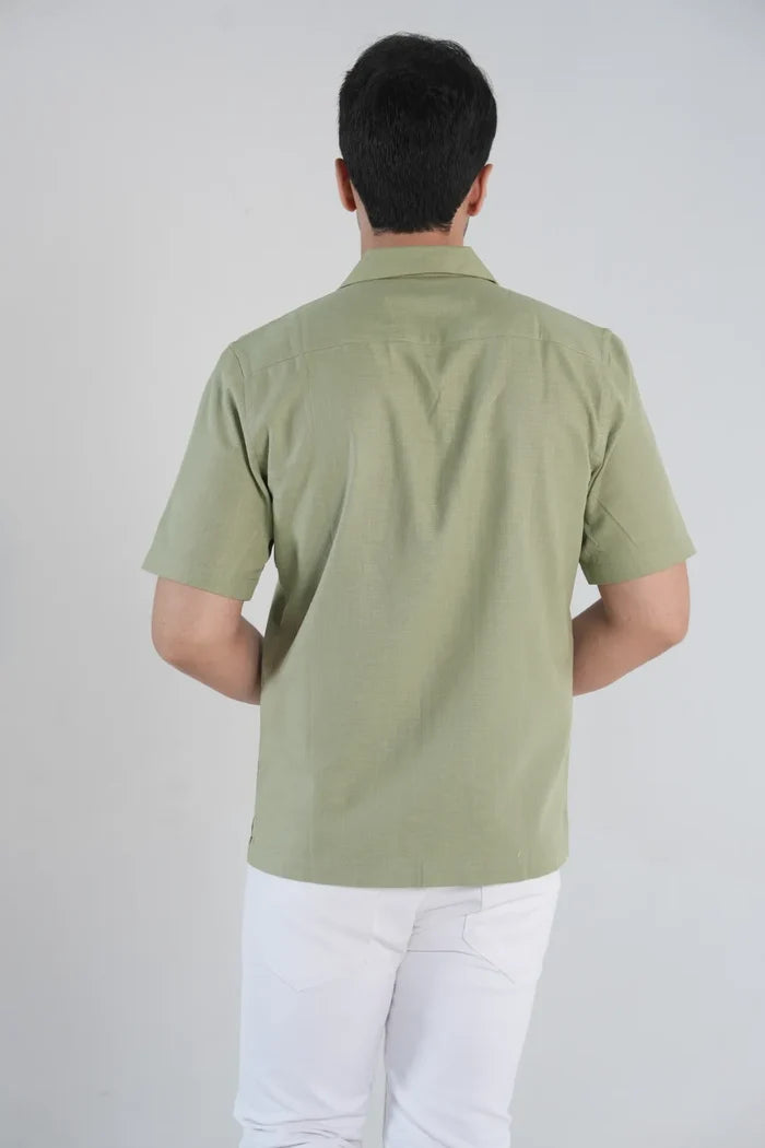 Person wearing a green polo shirt and white pants on a plain background, back view