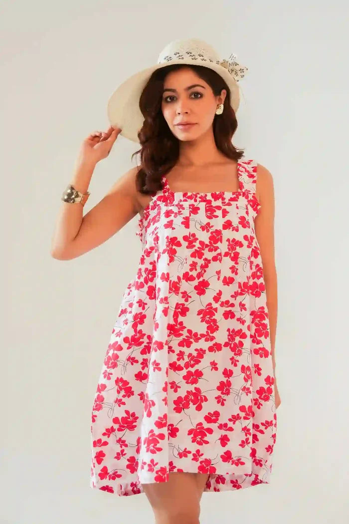 Woman in white and red floral cotton sundress with ruffle straps, styled with a wide-brim straw hat and metallic cuff bracelet — chic summer cottagecore outfit.
